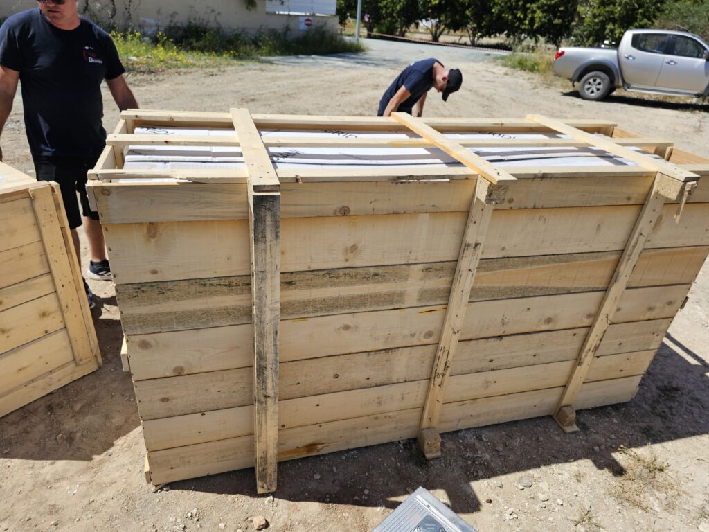 Professional movers securing high-tensile lifting straps around an oversized wooden furniture crate prior to an aerial lift.
