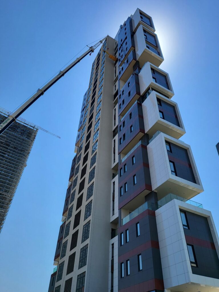 A towering crane lifting heavy furniture up the modern exterior facade of Only Tower in Limassol.